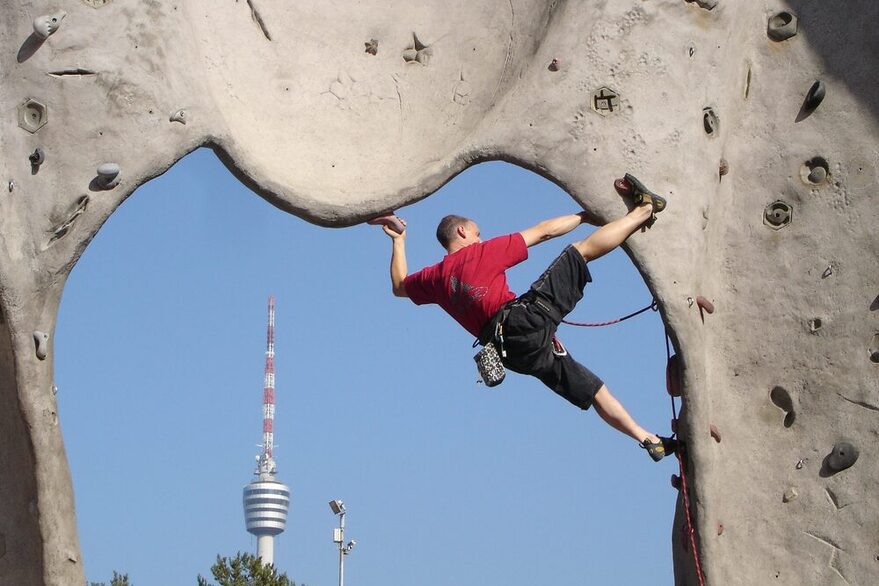 A man climbs a rock arch, the Stuttgart TV tower can be seen in the background.