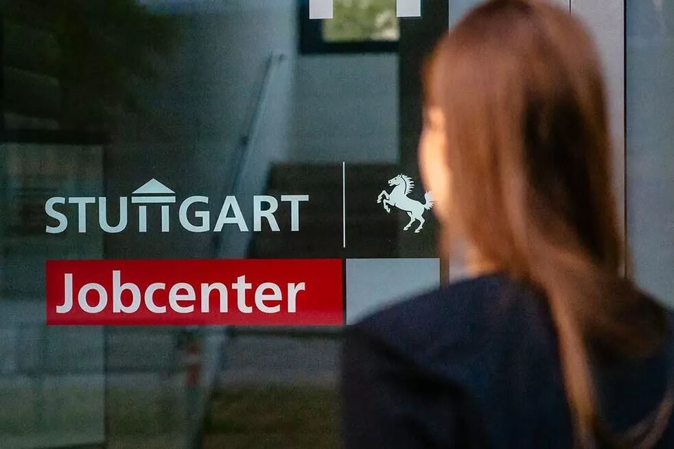 A Woman is standing in fornt of a glass door with the lettering "Stuttgart Jobcenter"
