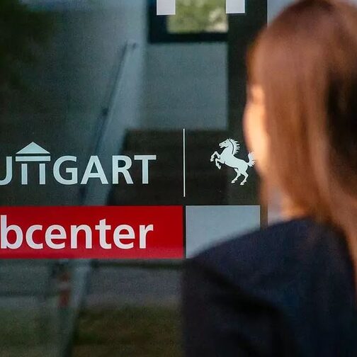 A Woman is standing in fornt of a glass door with the lettering "Stuttgart Jobcenter"